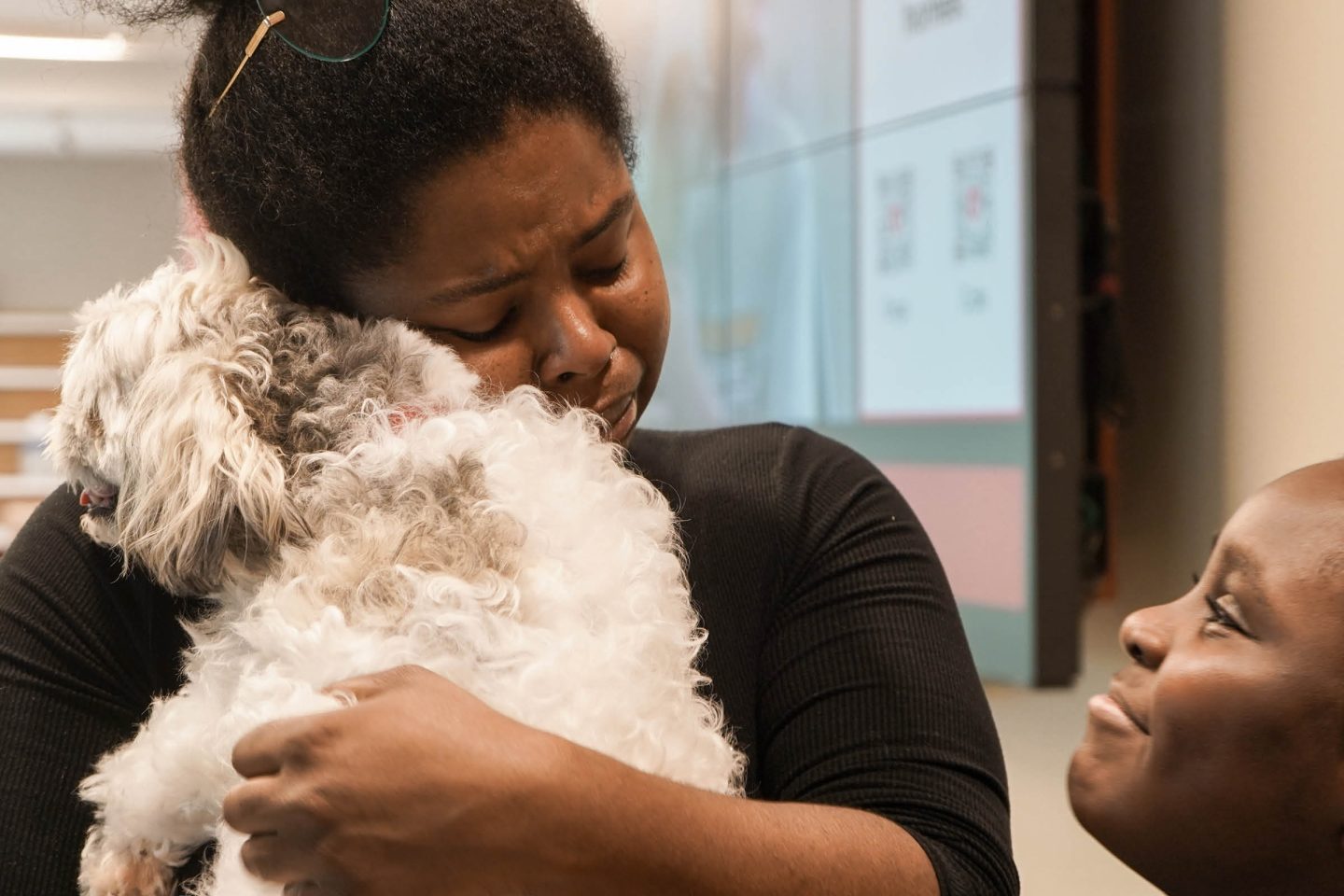 woman hugging a dog with a child smiling and looking on