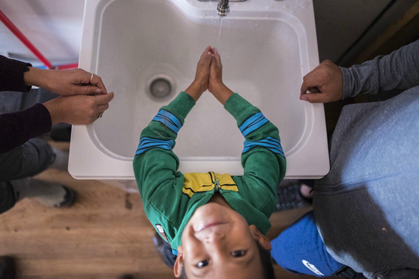 A smiling child looks at the camera while washing his hands