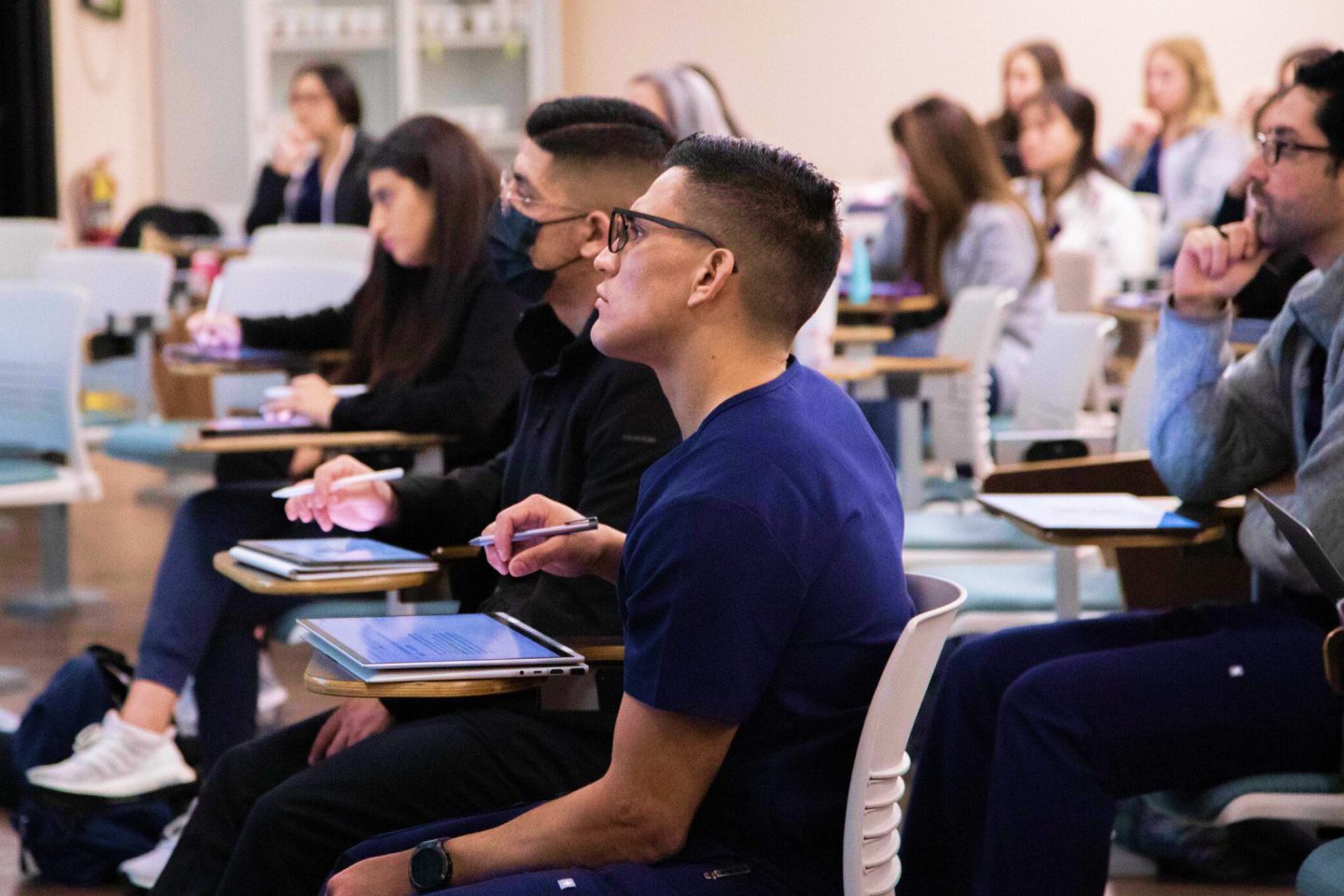 students in a class listening and taking notes on ipads