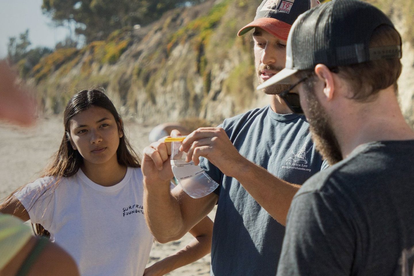 a woman and two men taking environmental action on the beach 