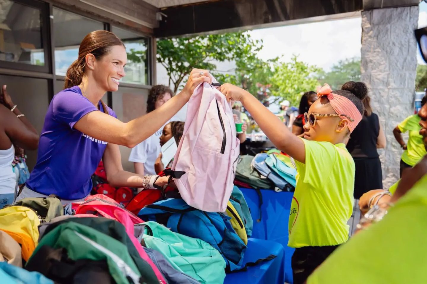 woman handing a child a backpack over a table of backpacks