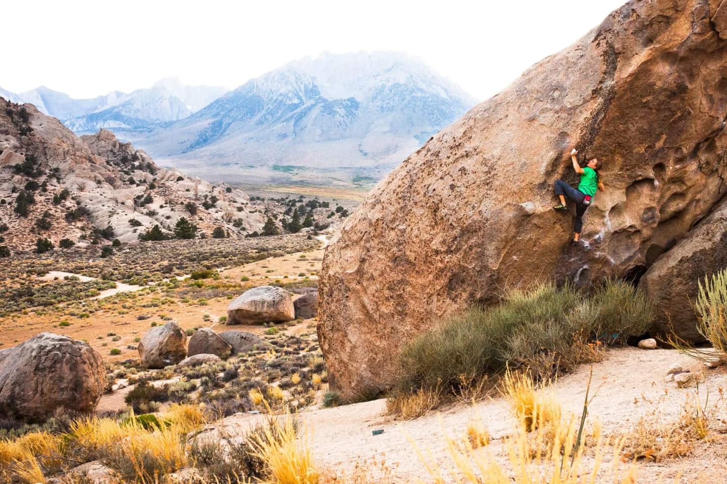 A rock climber ascends a boulder in a desert environment