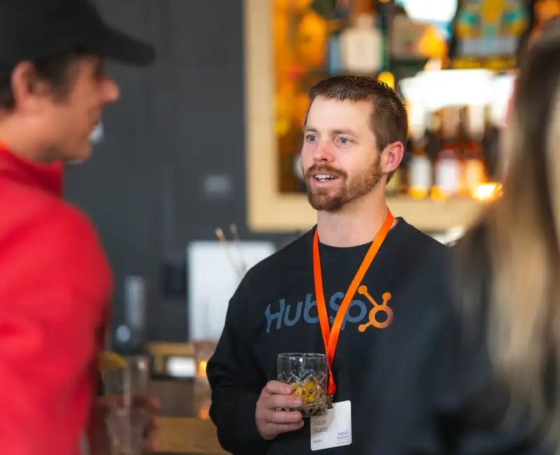 A man with a HubSpot shirt smiles at others in a bar