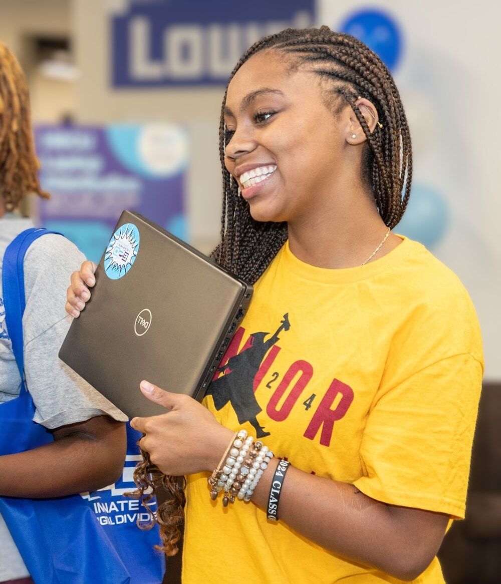 A smiling teenager holds up a new laptop