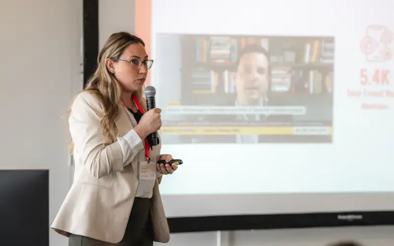 A woman holds a microphone and stands in front of a projector screen