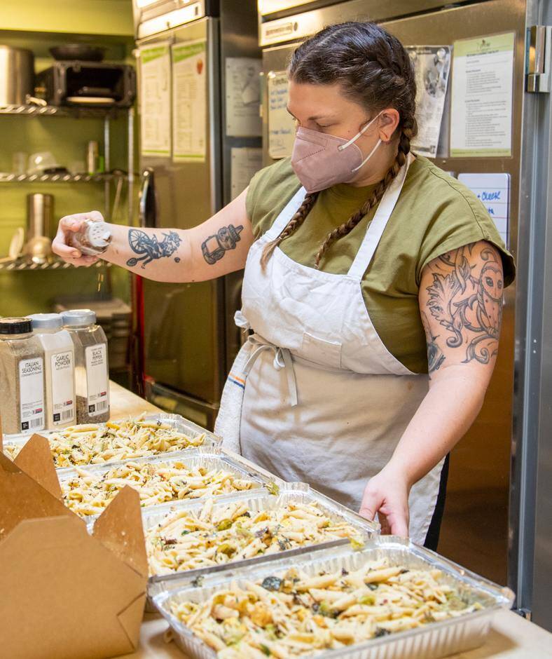 A woman adds spices to trays of pasta