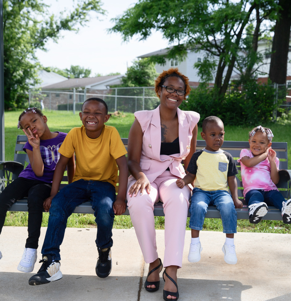 A mother and her four young children sit on a swing together.